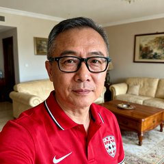一位中年男性球迷用户李铭的头像照片，他戴着眼镜，身穿红色足球POLO衫，背景是家中客厅